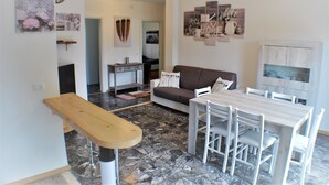 A modern living room with a sofa, dining table, and chairs, a kitchen area with a stove and cabinets, and a hallway leading to another room. - Entire apartment CASA FELICE 9 Places Free Parking and Free Wi-Fi Included (Venezia)