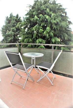Relax on the balcony with a pair of chairs and a table, surrounded by a lush tree.
