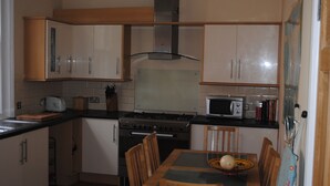Una cocina con armarios de madera, estufa, microondas y una mesa de comedor con sillas.