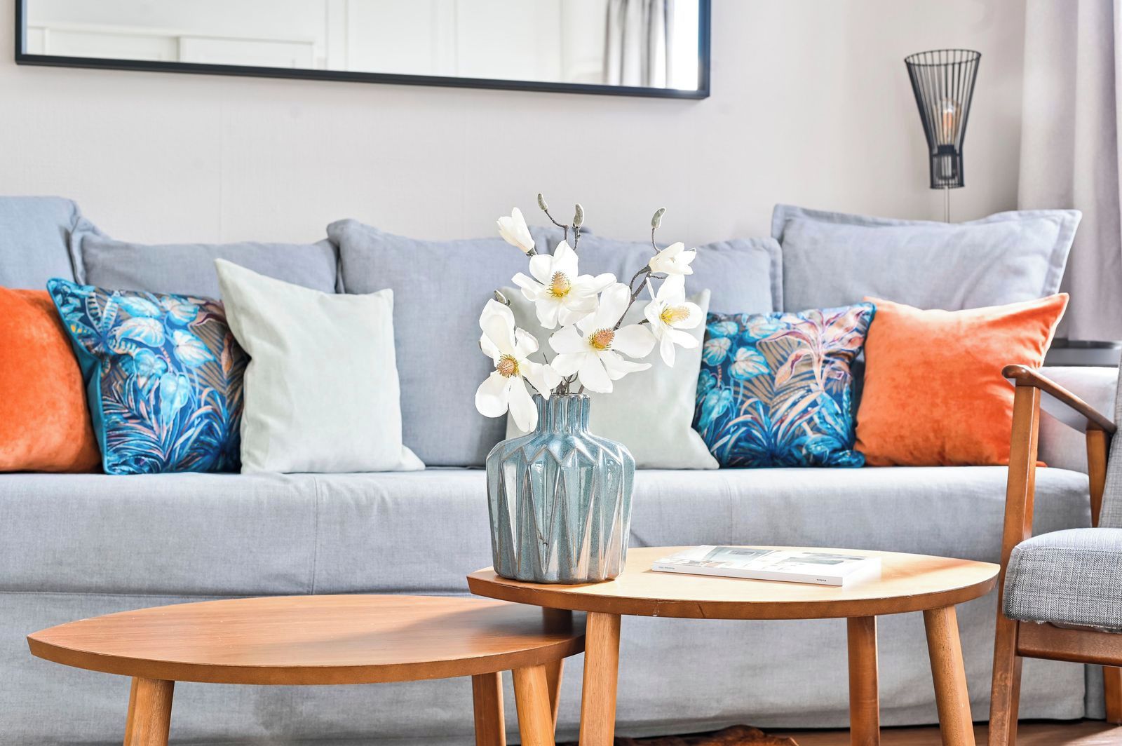 A living room with a grey sofa, a blue vase with white flowers, and a round wooden table.
