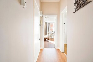 Un pasillo con piso de madera que lleva a una habitación con ventana y una mesa.