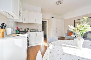 A modern kitchen with white cabinets, a dining table with a white tablecloth, and a vase with flowers.