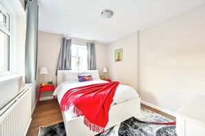 Un dormitorio con cama, mesitas de noche, una ventana con cortinas, un radiador y una alfombra.