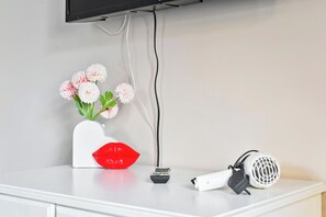 A white table with a vase of flowers, a red object resembling lips, a remote control, and a white device with a black cord.