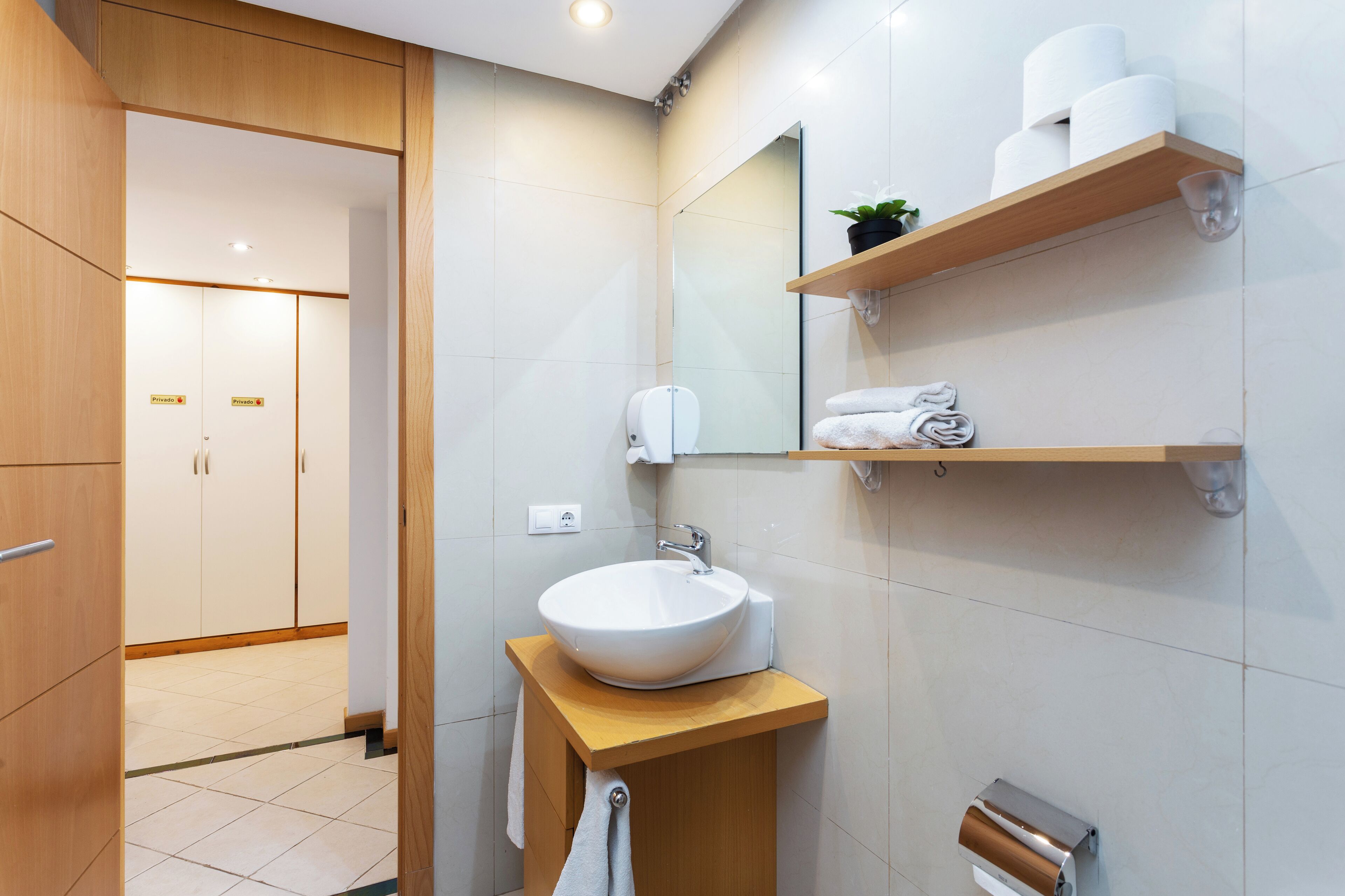 Une salle de bain moderne avec un lavabo blanc, un meuble-lavabo en bois et des étagères où sont rangés les produits de toilette.