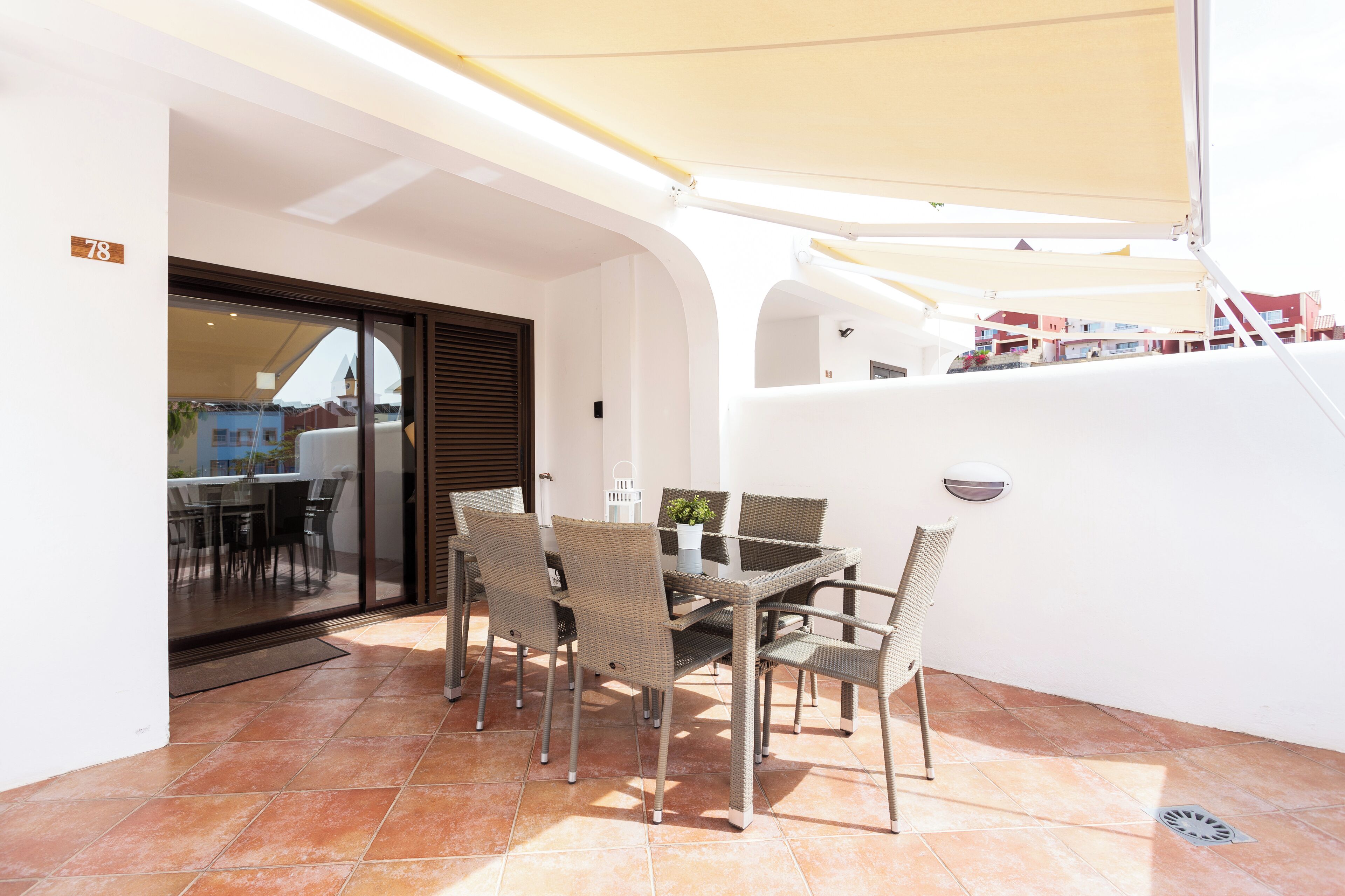 Un patio con mesa y sillas, una puerta corrediza de vidrio y una pared blanca.