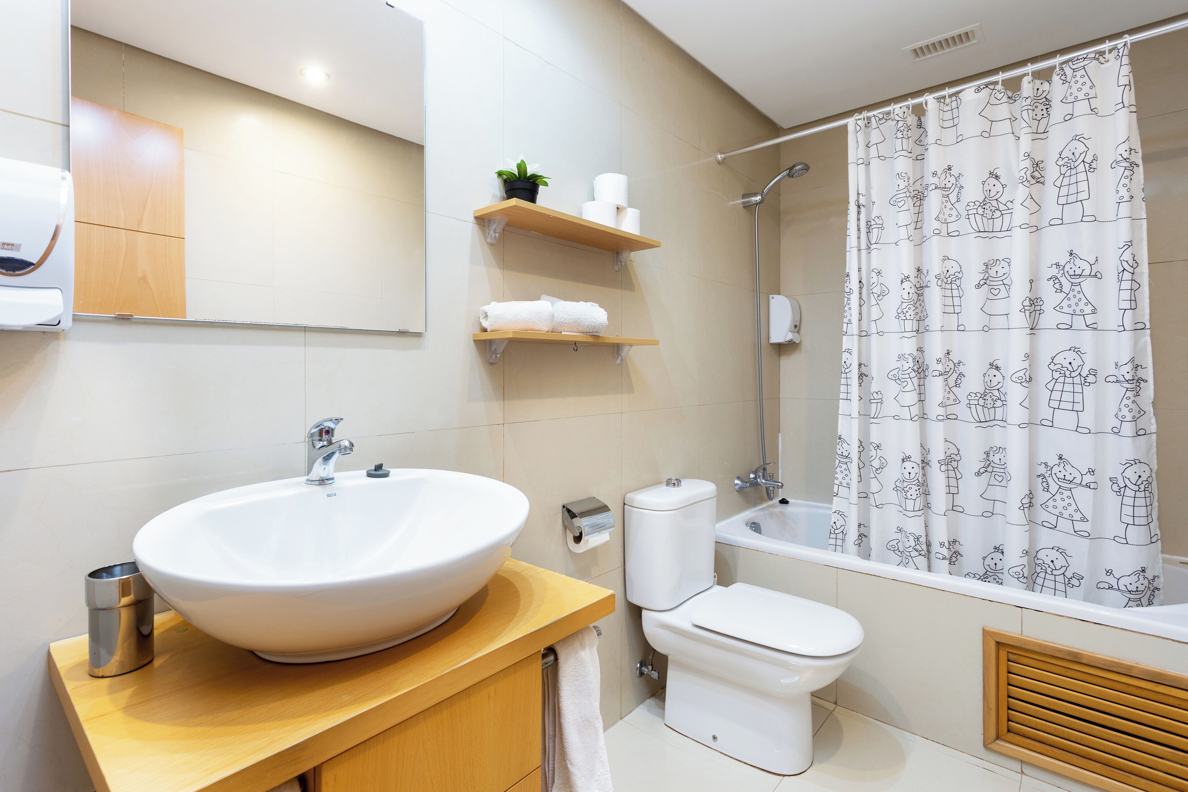 Een moderne badkamer met een grote witte wastafel, toilet en badkuip. Er zijn houten planken met handdoeken en een plant in pot.