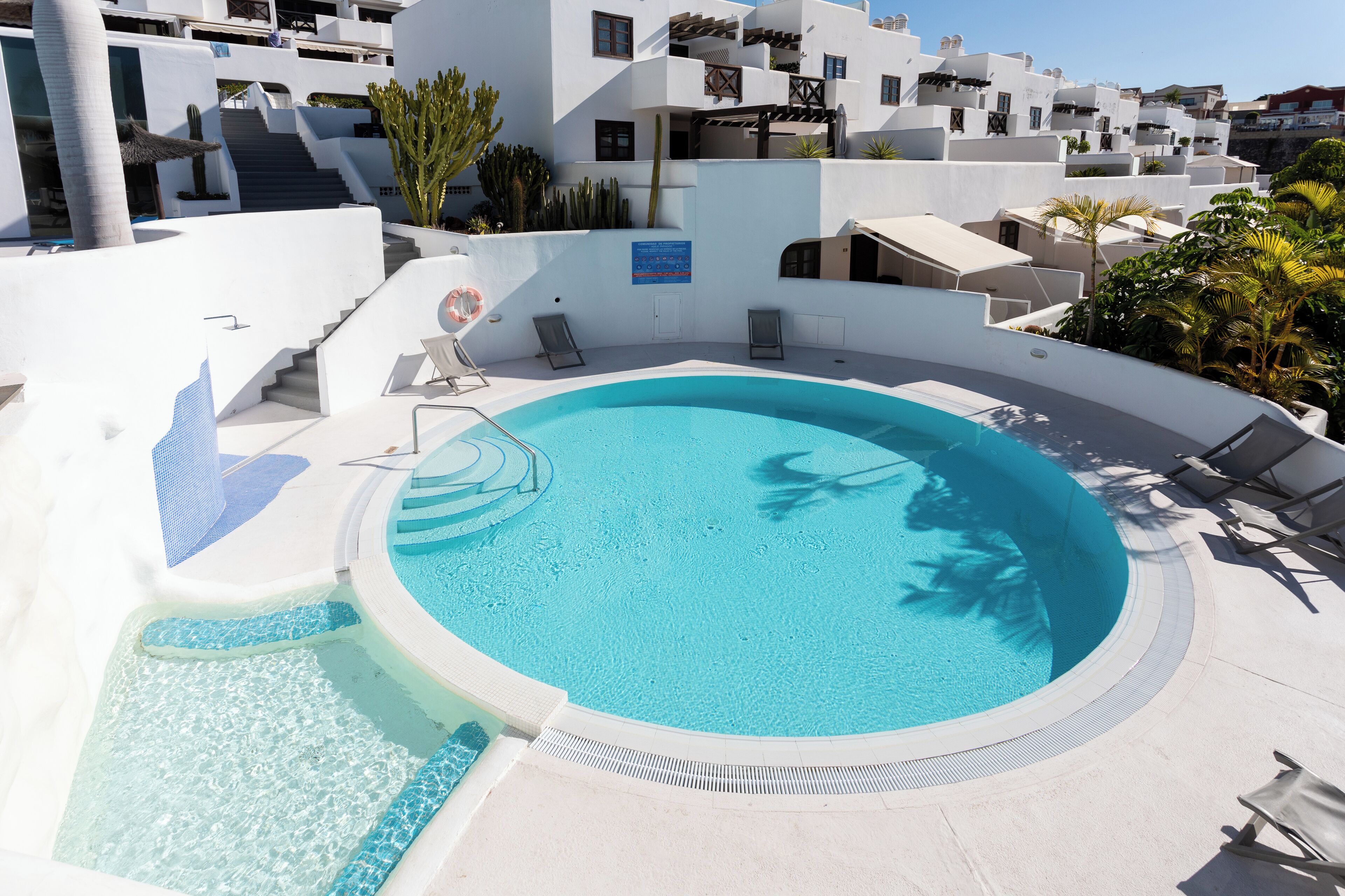 A pool area with a circular hot tub, lounge chairs, and a staircase leading to upper levels.