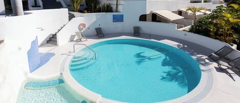 A pool area with a circular hot tub, lounge chairs, and a staircase leading to upper levels.