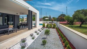 A modern outdoor patio with a pool, seating area, and a garden with gravel paths and shrubs. - This villa with pool is surrounded by nature and offers tennis court. (Sikici)