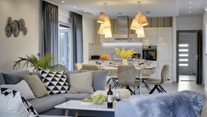 A modern living room with a sofa, dining table, and chairs. There is a kitchen in the background with a dining table and chairs. - This villa with pool is surrounded by nature and offers tennis court. (Sikici)