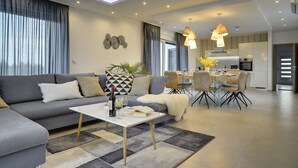 A modern living room with a grey sofa, a coffee table, and a dining area with chairs and a table. - This villa with pool is surrounded by nature and offers tennis court. (Sikici)