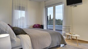 A modern bedroom with a large bed, a flat-screen TV mounted on the wall, and a balcony with a view. - This villa with pool is surrounded by nature and offers tennis court. (Sikici)