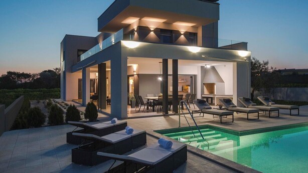 A modern two-story house with a swimming pool, outdoor seating, and a patio area. - This villa with pool is surrounded by nature and offers tennis court. (Sikici)
