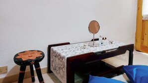 Une petite pièce avec un lit en bois, une table de chevet avec un miroir et un petit tabouret.