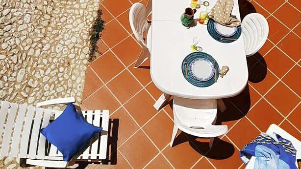 Une terrasse avec une table blanche dressée pour quatre personnes, entourée de chaises blanches.