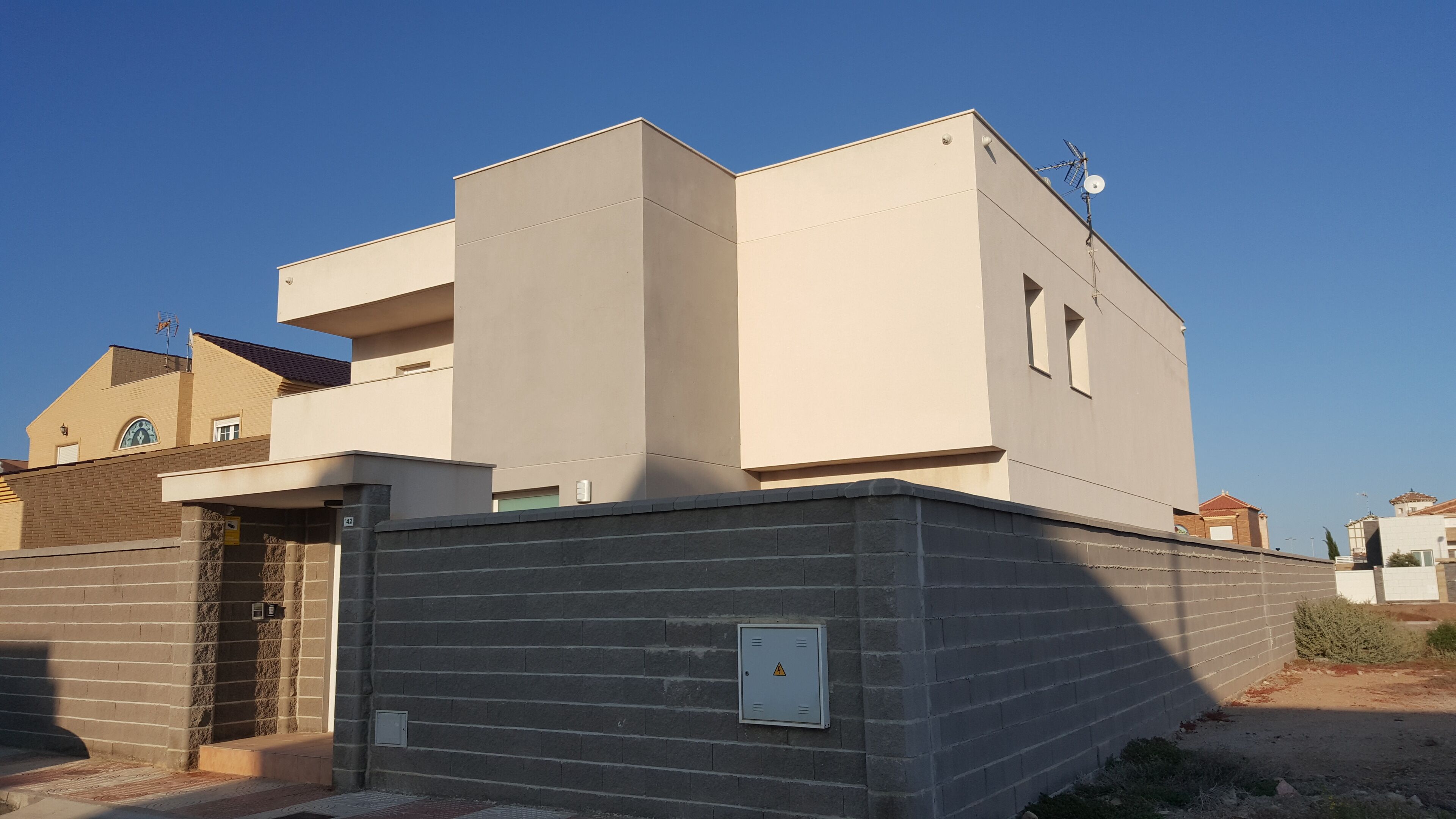 Een modern gebouw met twee verdiepingen, een plat dak, een klein balkon en een bakstenen entree.