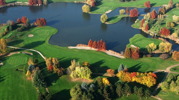 Un campo de golf con varios estanques, bunkers de arena y árboles de colores otoñales.