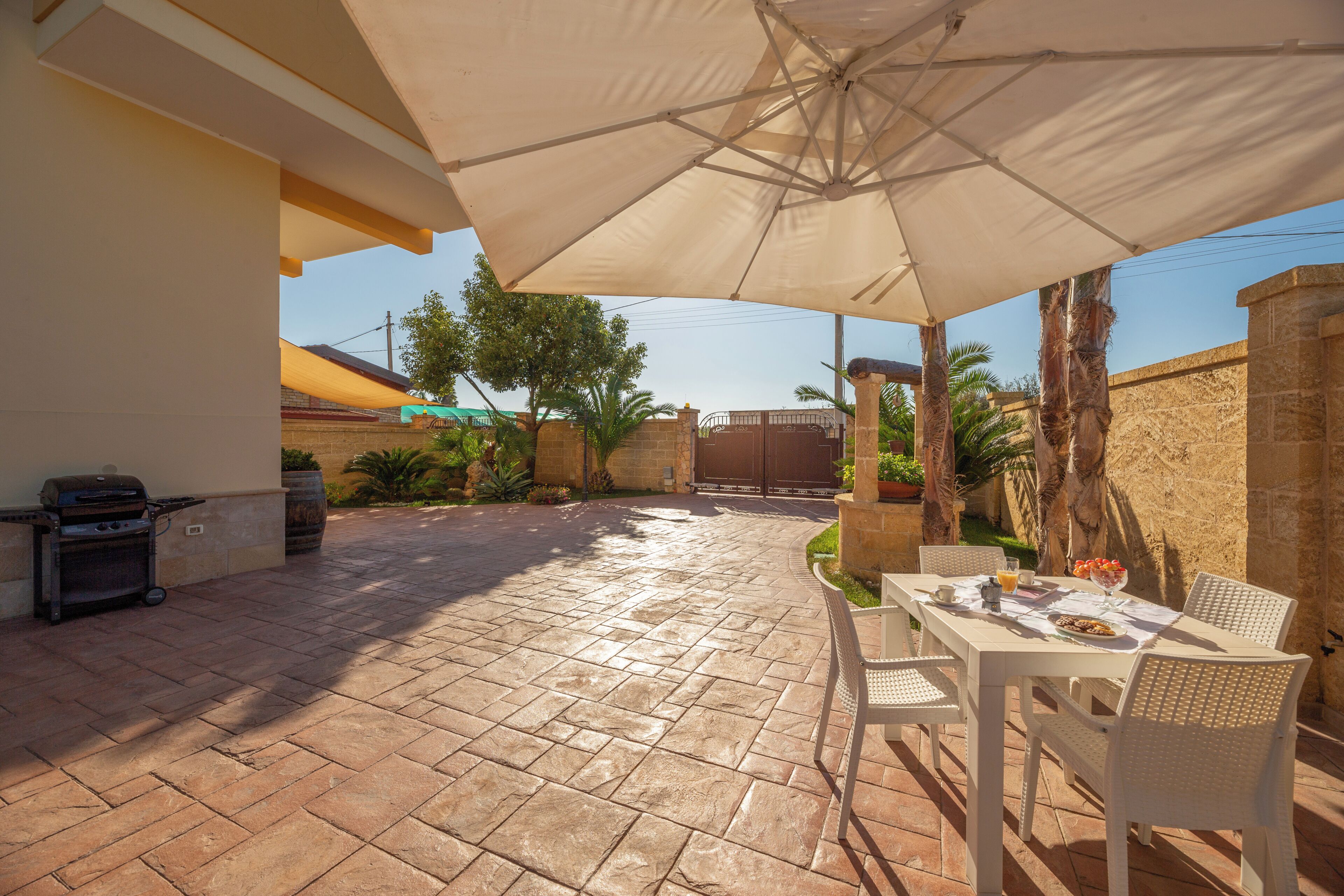 Eine Terrasse im Freien mit Tisch, Stühlen, einem Grill und einem großen Sonnenschirm.
