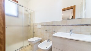 Een badkamer met een douchecabine van glas, een toilet, een bidet en een wastafel met spiegel erboven.