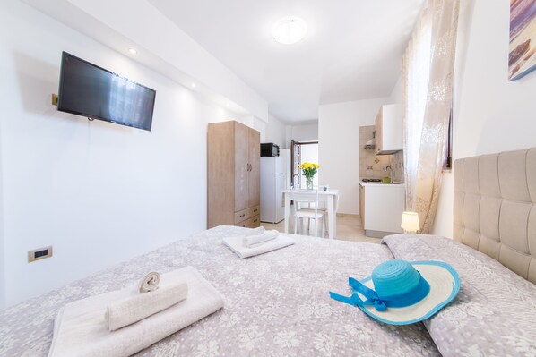 Ein modernes Hotelzimmer mit Flachbildfernseher, einem Bett mit blauem Hut, einem Schreibtisch und einer Küchenzeile.