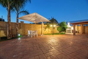Eine Terrasse im Freien mit Steinböden, einem Tisch mit Stühlen und einem großen Sonnenschirm.