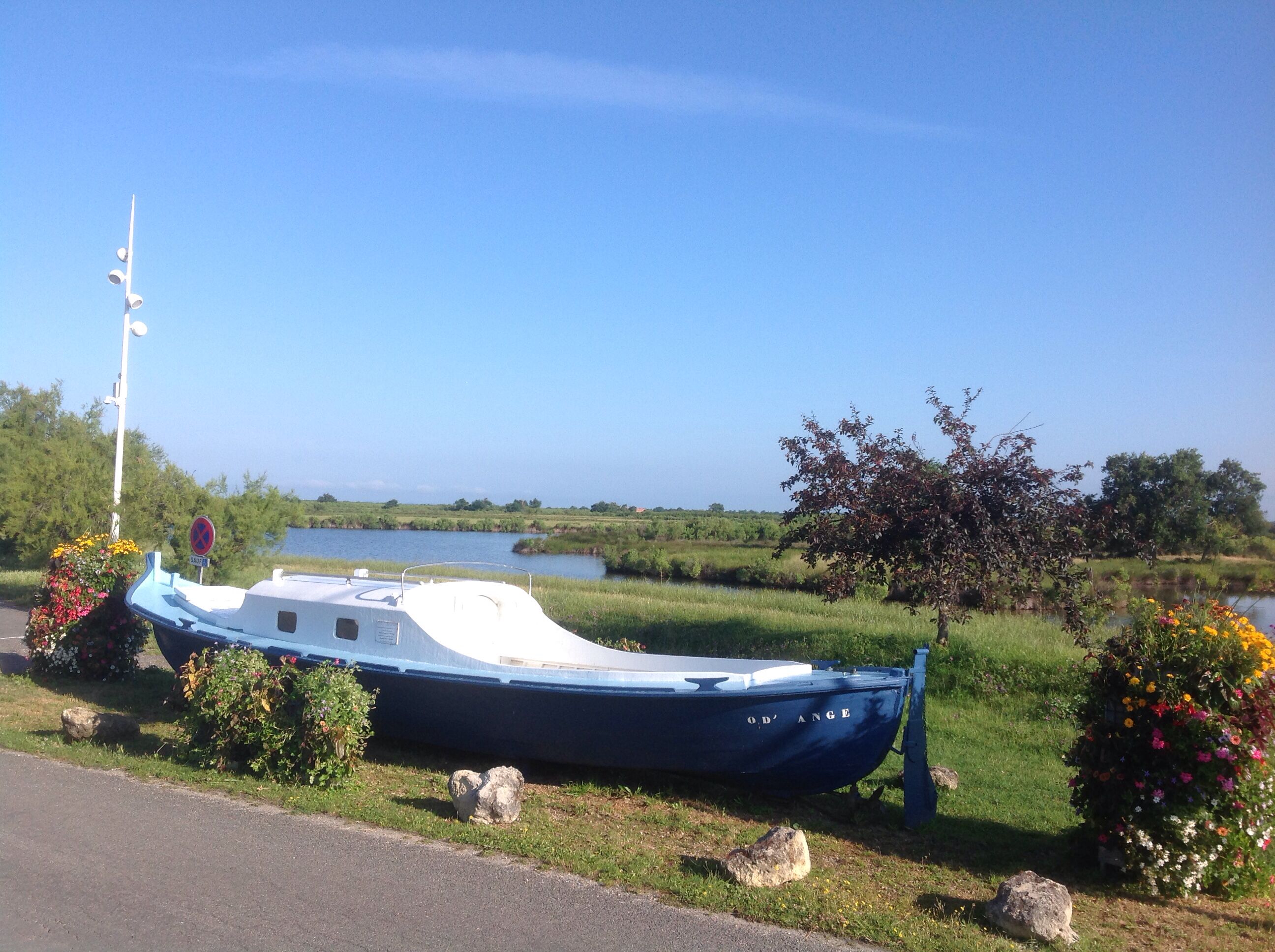 A boat named "OD' ANGE" docked near a river with a clear sky.
