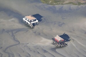 An aerial view of a coastal area with two buildings on stilts, surrounded by sandbanks and water channels.