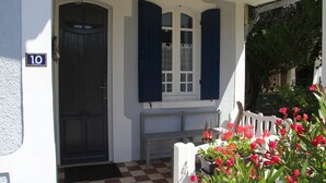 Entrada d'una casa amb un senyal de número, una porta, una banca i plantes en testos.