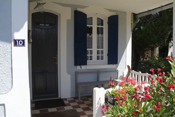 A house entrance with a number sign, a door, a bench, and potted plants.