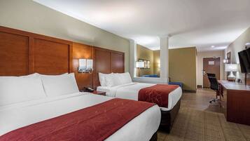 A hotel room with two beds, a desk, a chair, and a TV.
