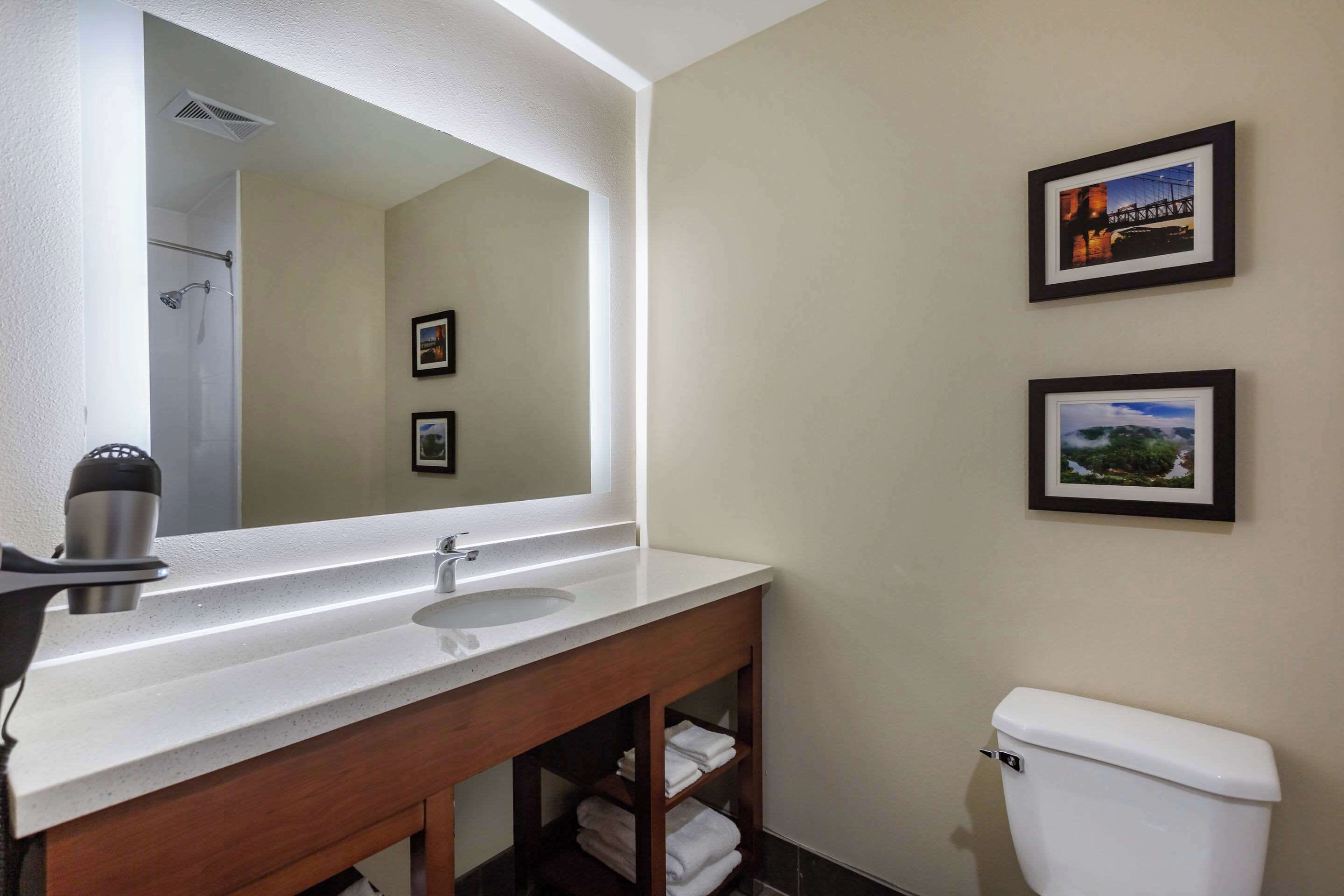 A bathroom with a white sink, a mirror, a toilet, and two framed pictures on the wall.