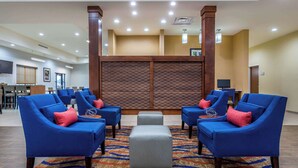 Un hall d’entrée avec des fauteuils bleus, un pouf gris et un tapis à motifs.