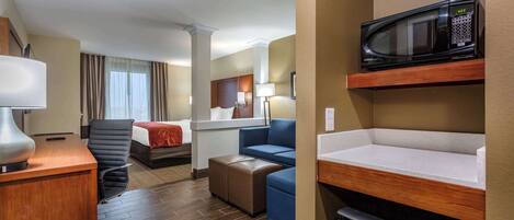 A hotel room with a desk, chair, sofa, and a microwave on a shelf.