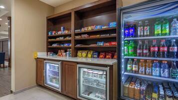 Estación de bebidas autoservicio con opciones refrigeradas y sin refrigerar, incluyendo gaseosas, jugos y agua embotellada.