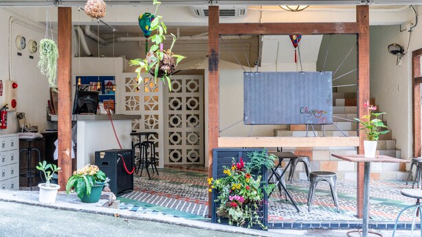 A cafe with outdoor seating, a wooden counter, and various plants.