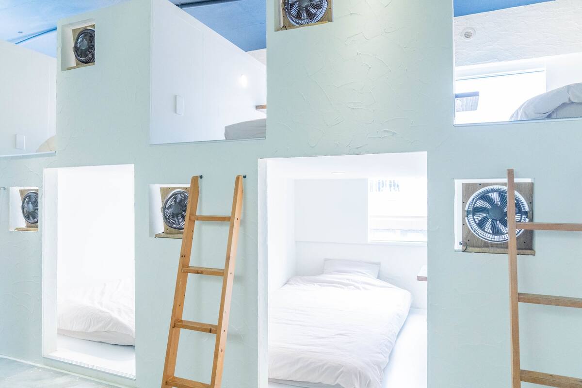 Une chambre avec des lits superposés, une échelle et des ventilateurs fixés au mur.