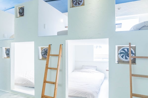 A room with bunk beds, a ladder, and wall-mounted fans.