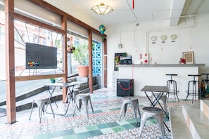 A cafe with a tiled floor, metal stools, a counter with a coffee machine, and a window with a view of the street.