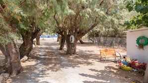 A pathway lined with trees, a wooden bench, and a wall with a wreath and flowers. - Villa Aadonis in the sea (Chania kolibari)