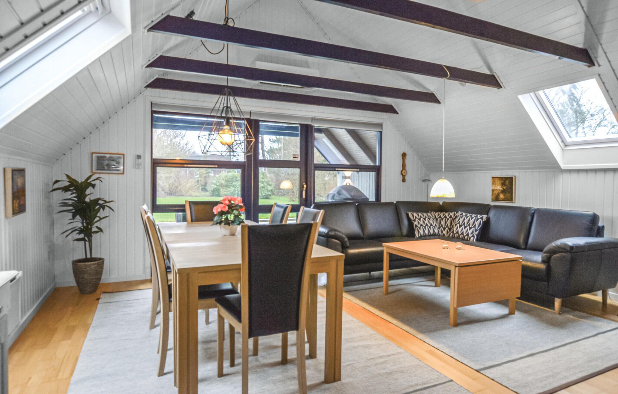 Un loft spacieux avec de hauts plafonds, des poutres apparentes, un coin repas avec une table et des chaises, un canapé et une grande fenêtre donnant sur l’extérieur.