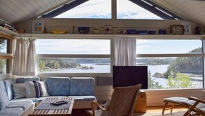 A cozy room with a large window overlooking a lake, a sofa, a wooden table, and a TV. - 4 bedroom beautiful home in Tvedestrand (Tvedestrand)