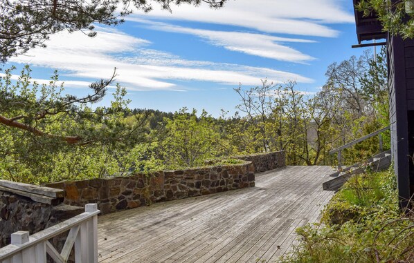 A wooden deck with a stone wall, surrounded by trees and a clear sky.