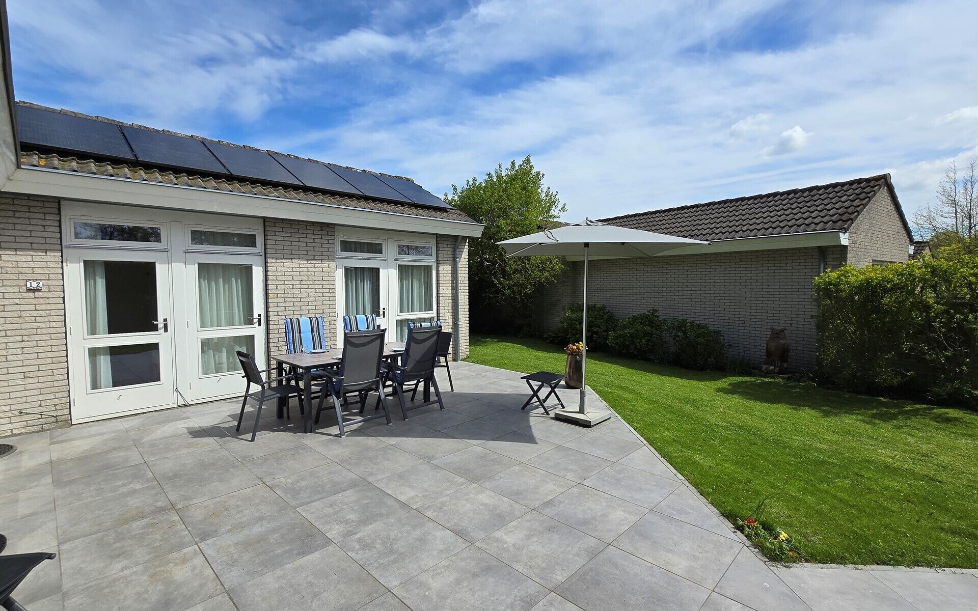 A patio area with a table and chairs, a covered umbrella, and a brick building with a tiled roof.