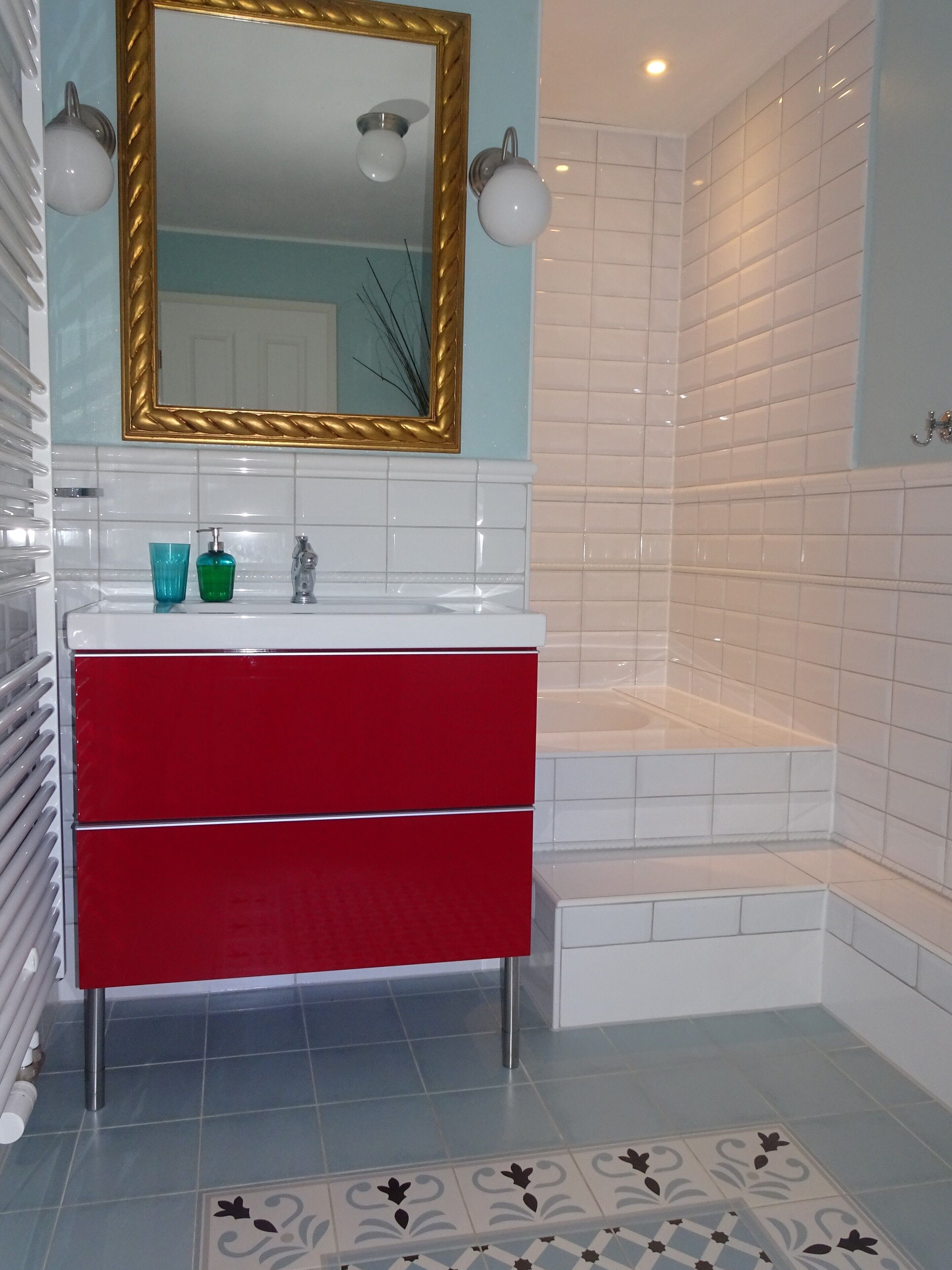 A modern bathroom with a white sink, red vanity, and a gold-framed mirror.