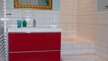 A modern bathroom with a white sink, red vanity, and a gold-framed mirror.