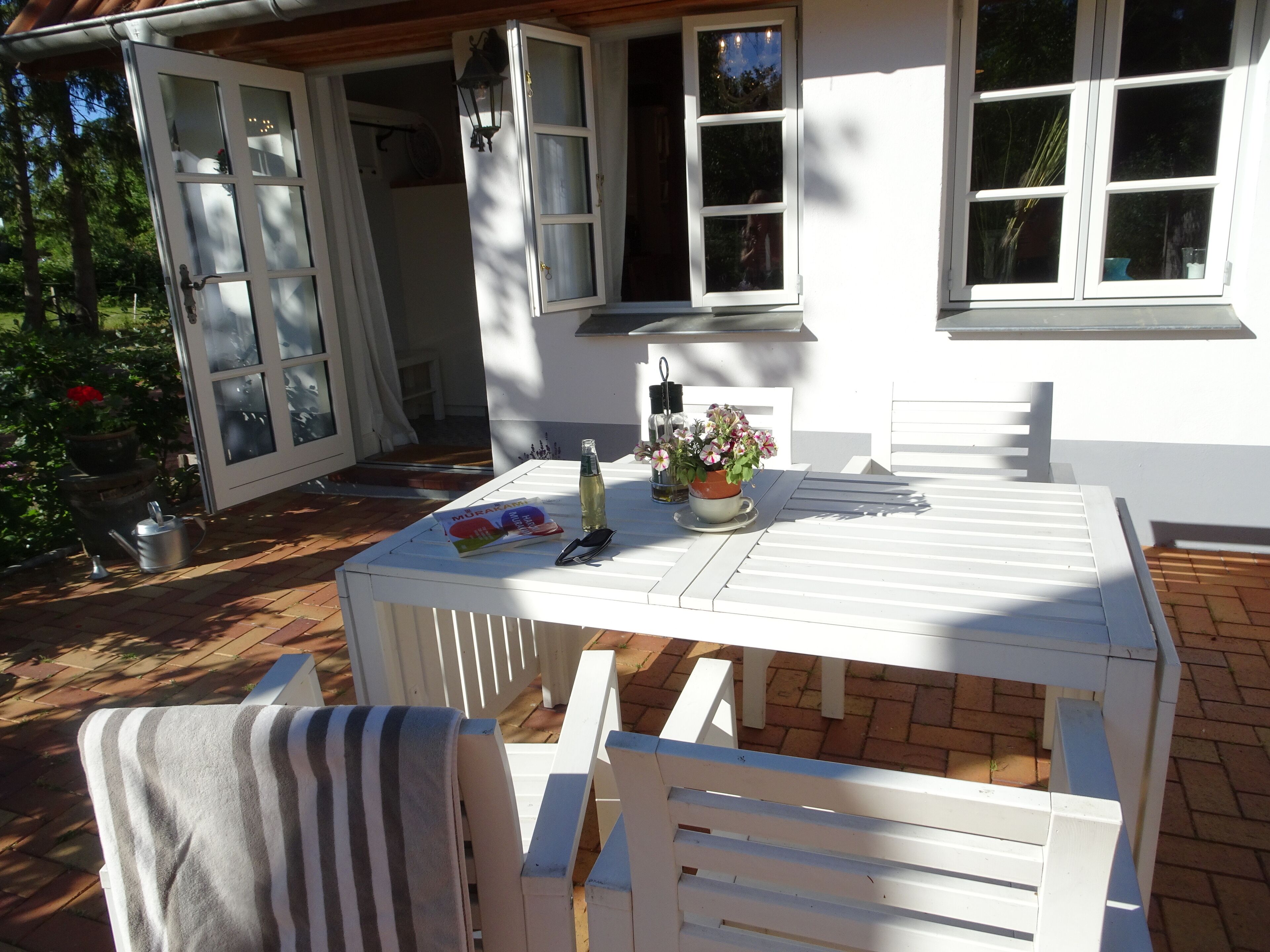 Ein weißer Tisch mit Stühlen, einer Flasche und einer Blumenarrangements auf einer Terrasse.