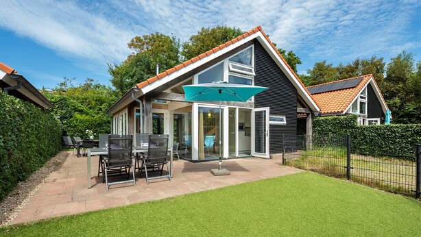 Une maison moderne dotée d’une grande porte vitrée, d’un espace salon extérieur et d’une pelouse bien entretenue.