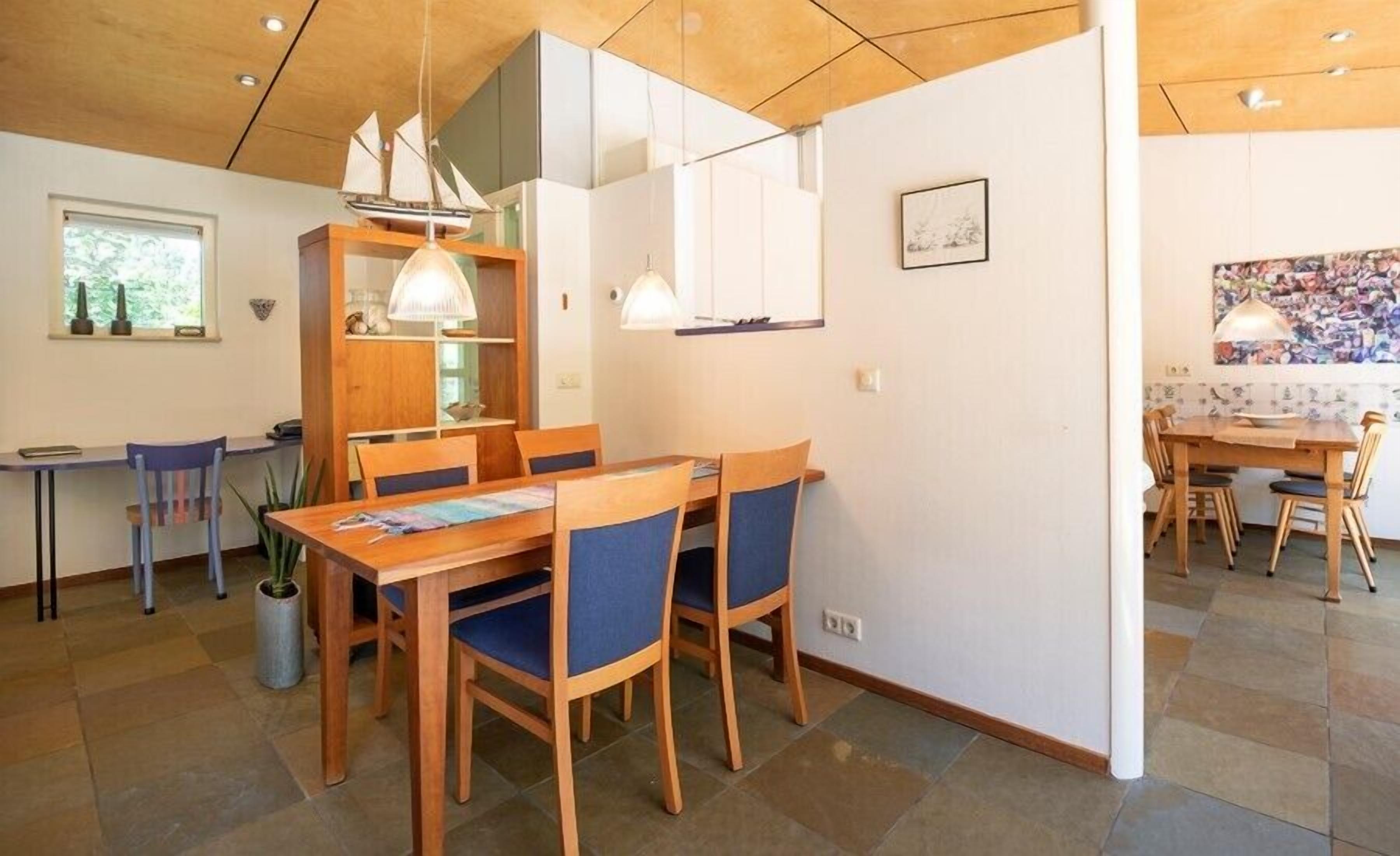 Un espace repas avec des tables et des chaises en bois, des luminaires suspendus et une vue sur l’extérieur par une fenêtre.