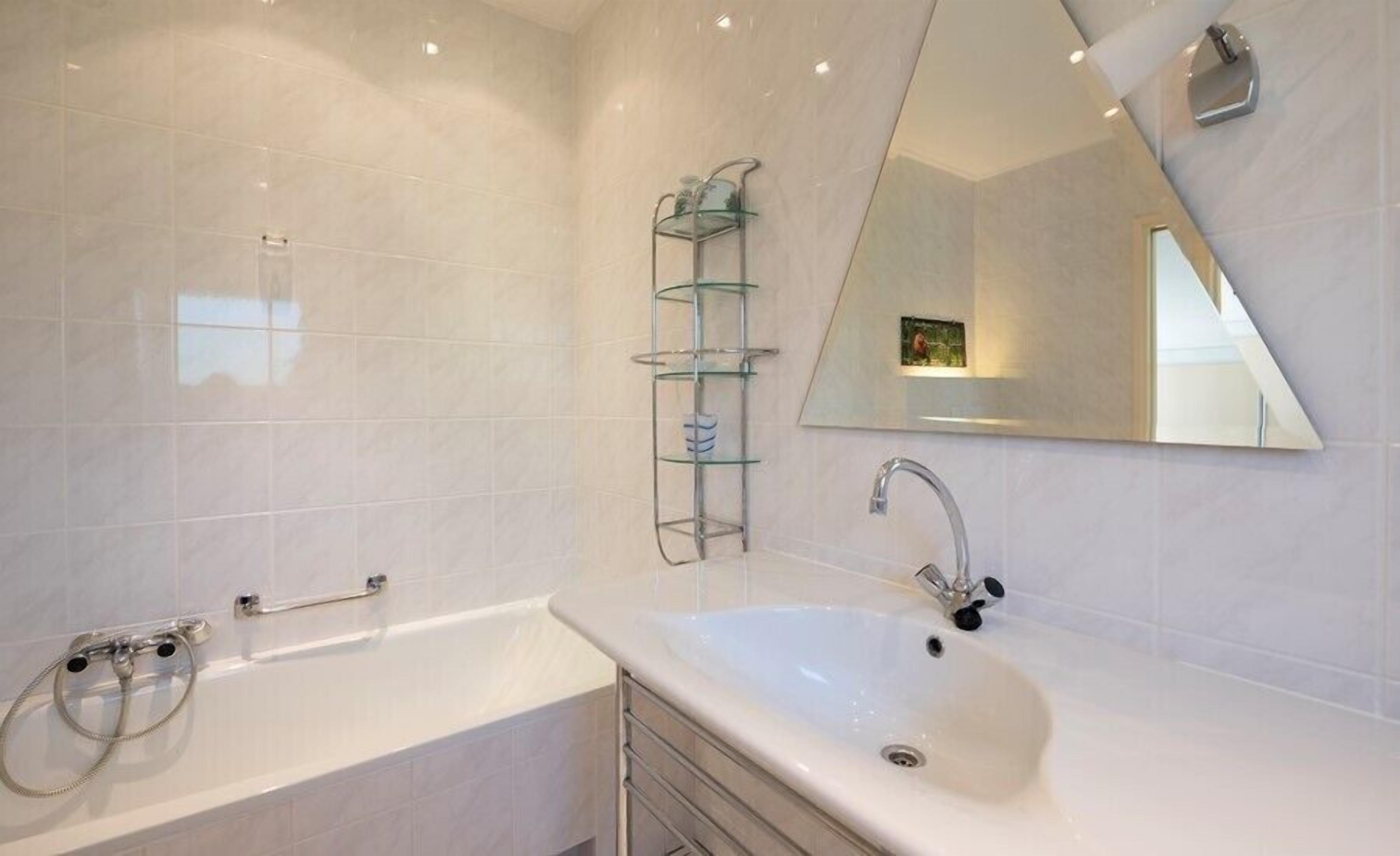 A modern bathroom with a white bathtub, a glass shelf unit, and a large mirror.